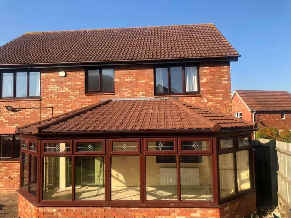 Red brick house with a glass conservatory on a clear day, featuring granulated brown Lightweight Tiles