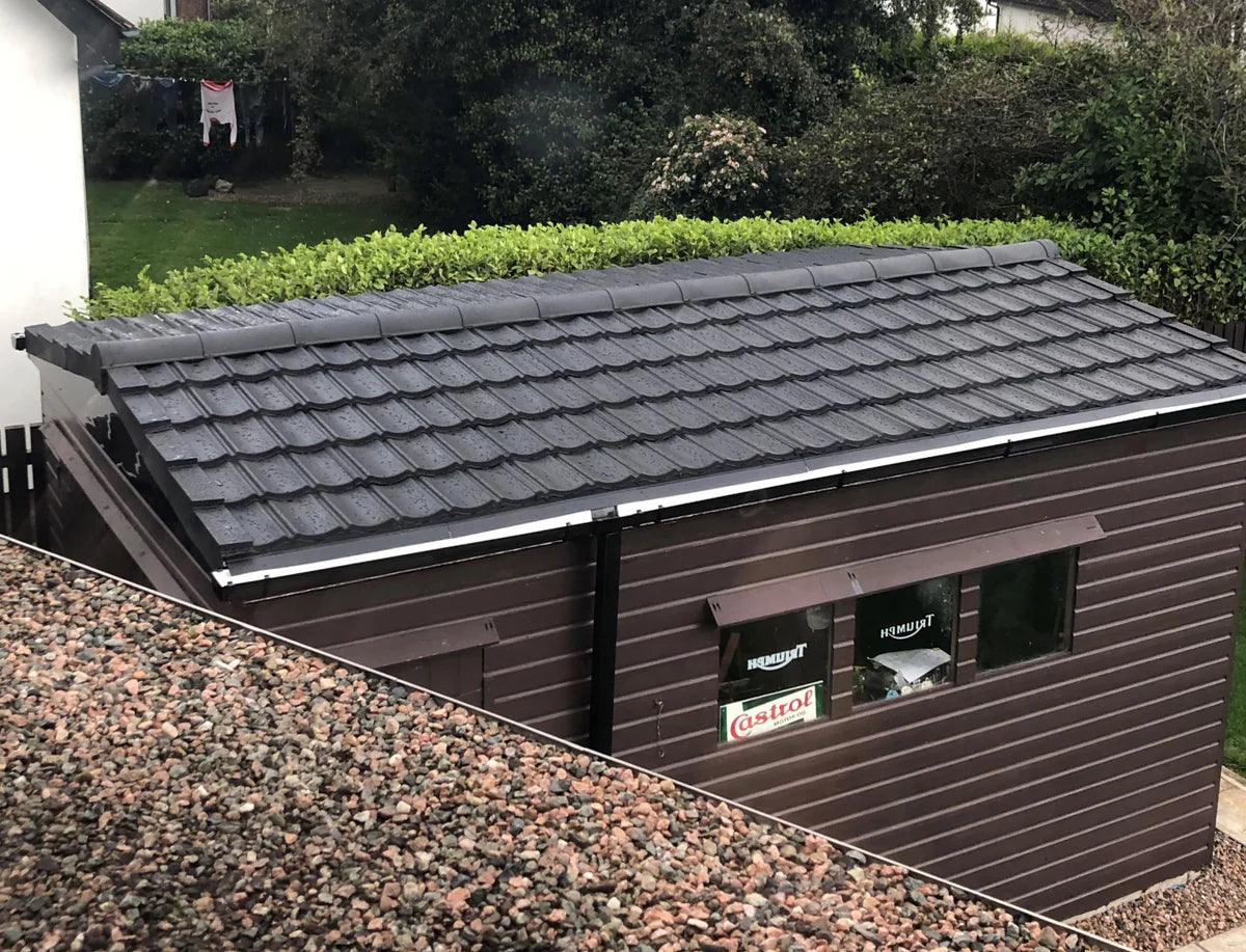 A dark brown shed with a smooth black lightweight tiled roof, seen from an elevated perspective.