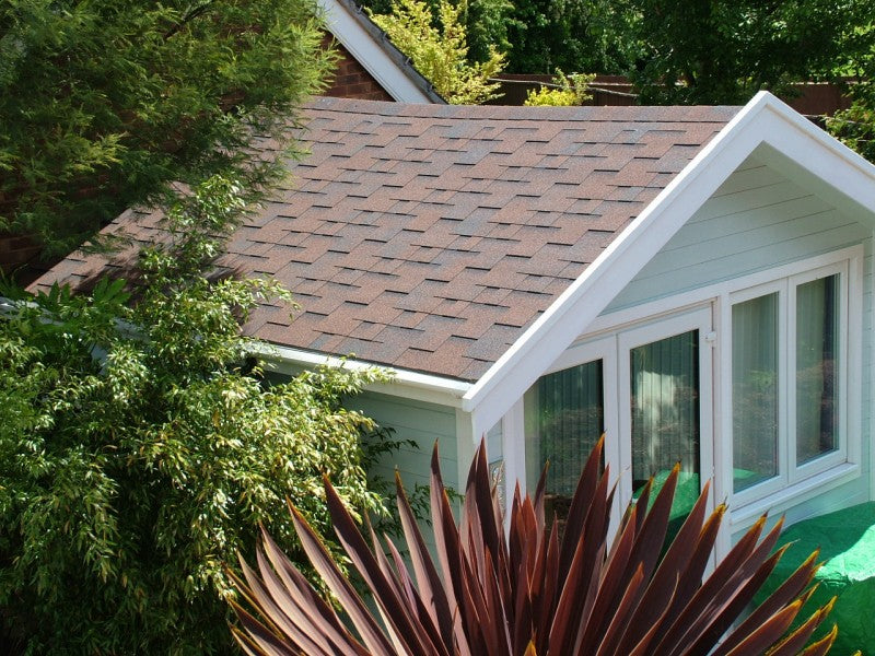 House with a brown roof and white trim, surrounded by greenery