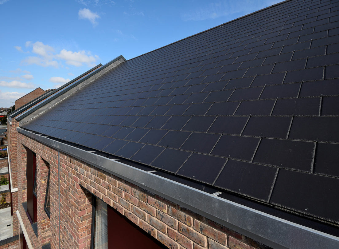 Close up of black roof slates on a red brick house with a blue sky in the background
