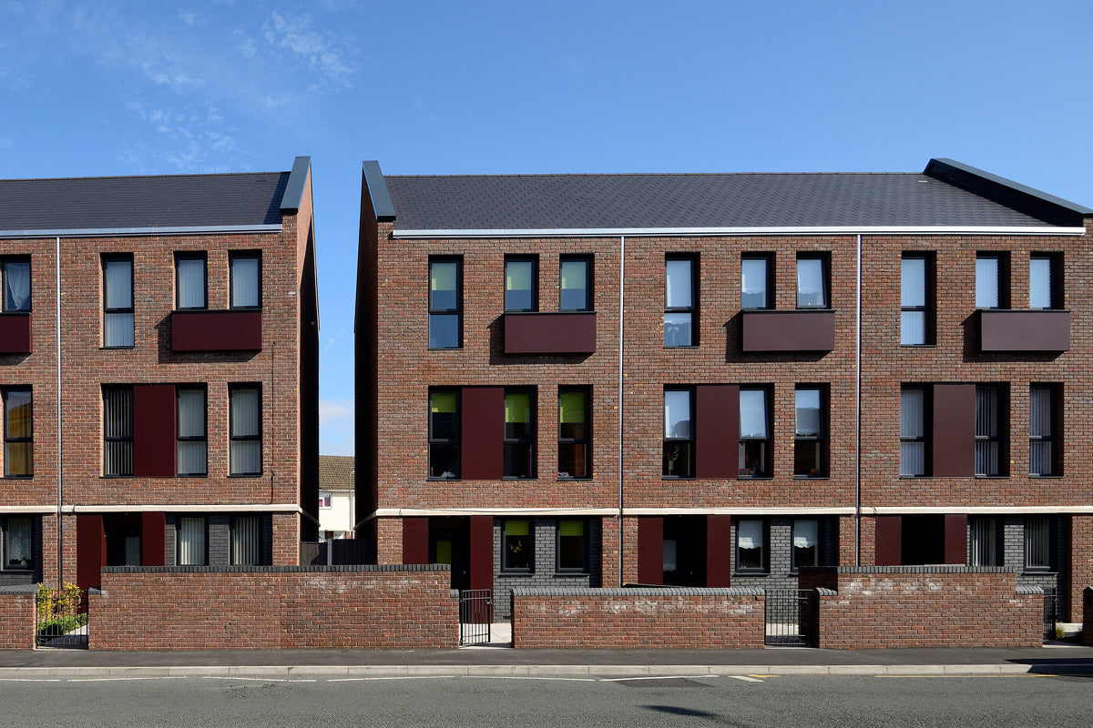 Row of modern brick apartment buildings with black roof slates and a blue sky in the background