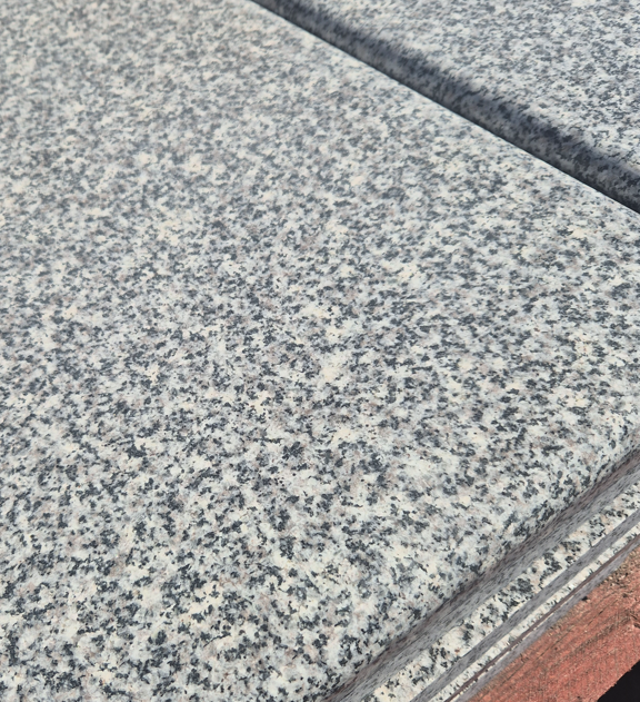 Close up in situ Castle Dolomite Grey granite coping stone installed on a garden wall showing crisp edges and contemporary grey tones