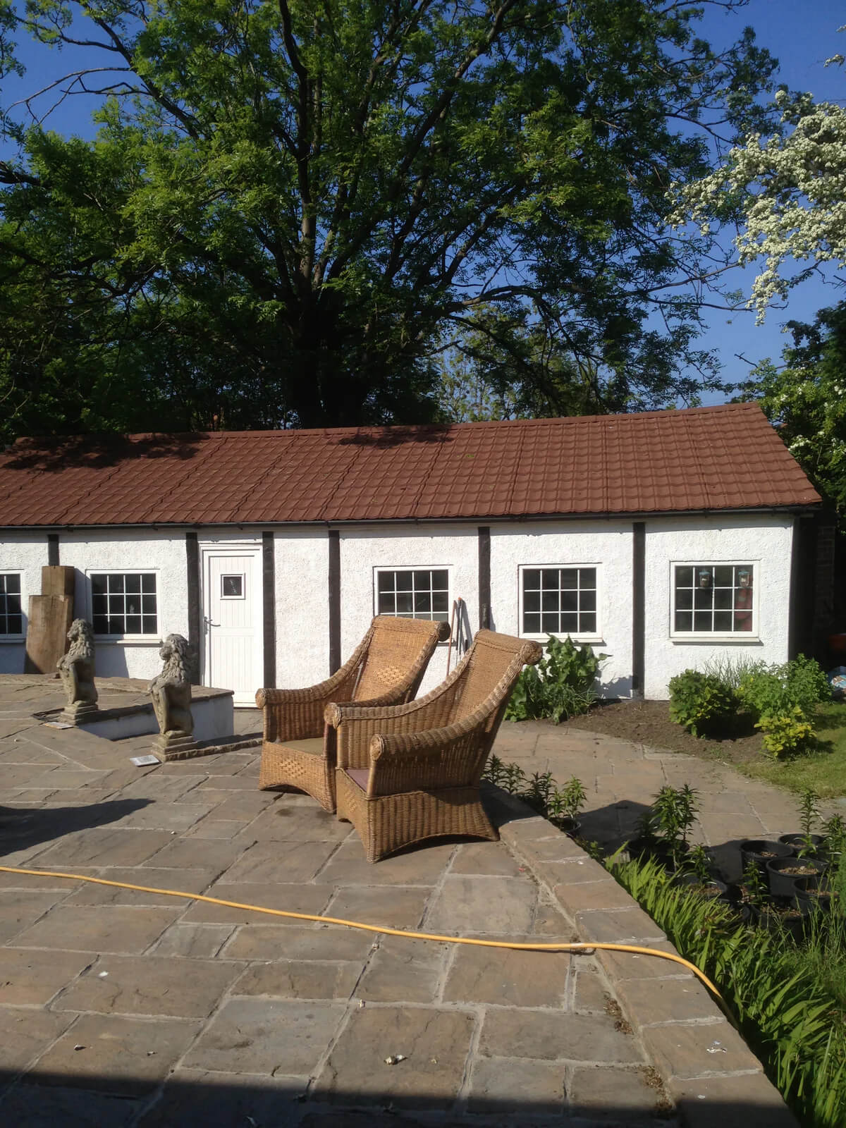 Outdoor patio area with wicker chairs, garden hose, and white office with granulated brown Lightweight Tiles on its roof