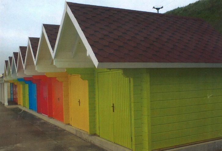Row of colorful wooden beach huts with red roofs.