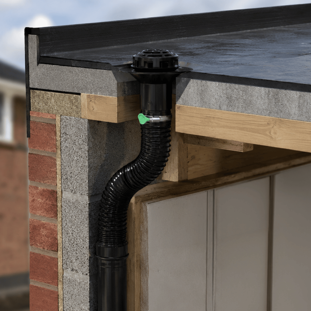 Black flexible downpipe with a green-handled valve attached to a roof gutter over a brick and concrete wall corner.