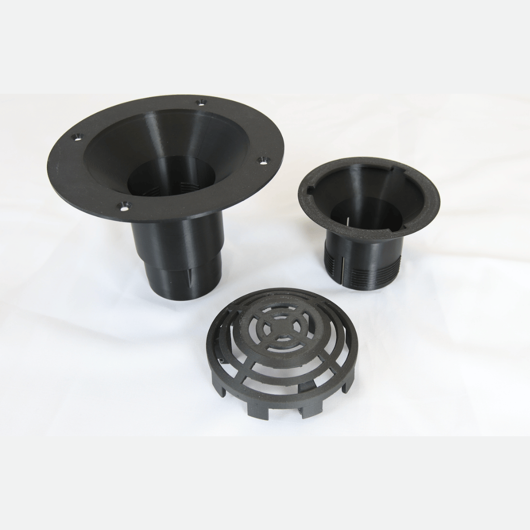 Three black plastic drainage components, including two flanged pipe sections and a circular grate cover, displayed on a white fabric background.