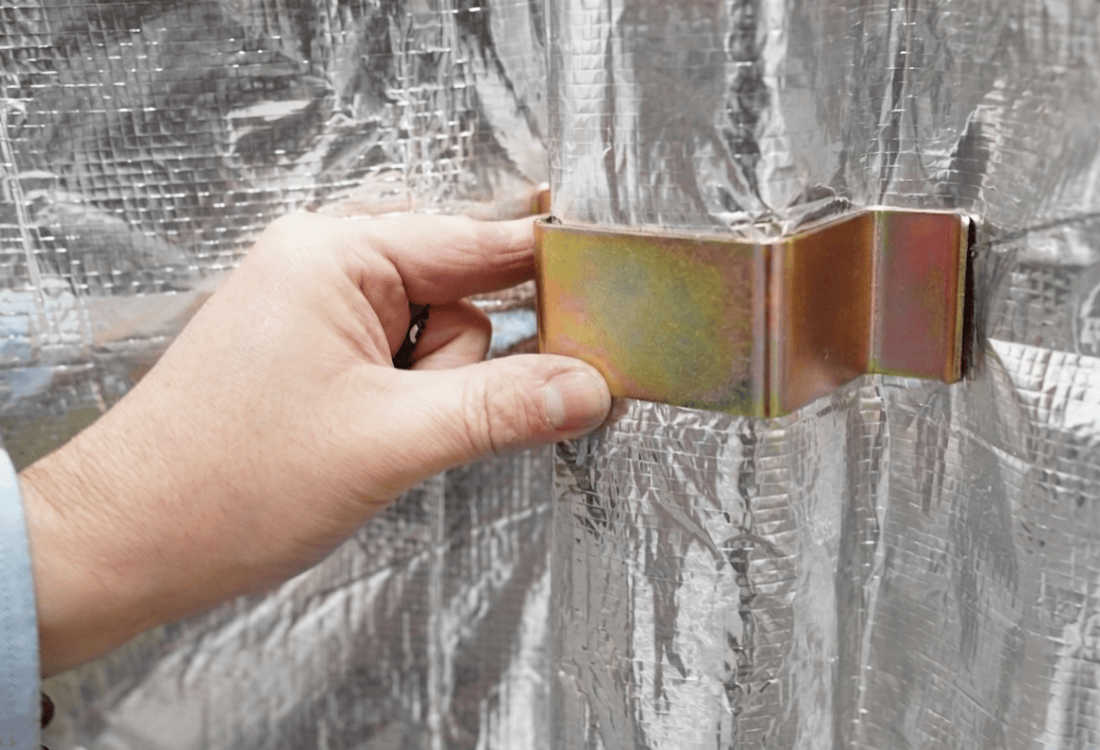 Hand holding a spacer against a textured silver foil insulation