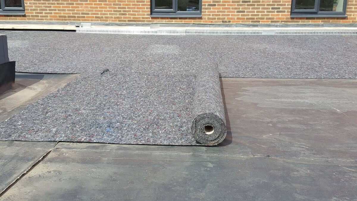 Roll of Wallbarn Polyester Geotextile on a flat roof with a brick building in the background